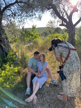 Photographer leaning over to take pictures of man and woman embracing, sitting on the grass. High quality photo