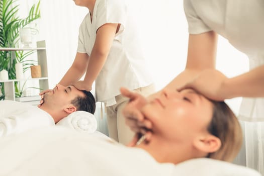Caucasian couple enjoying relaxing anti-stress head massage and pampering facial beauty skin recreation leisure in dayspa modern light ambient at luxury resort or hotel spa salon. Quiescent