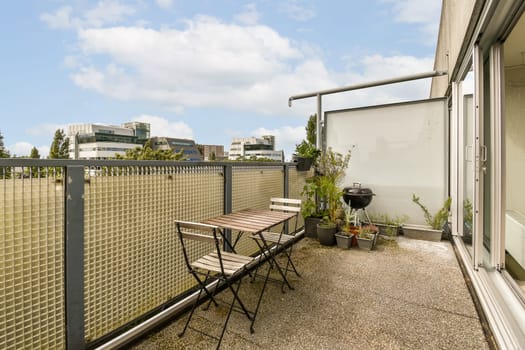 an outside area with a table, chairs and grill on the ground in front of a fenced off building