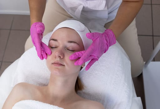 Young Woman Receives Spa Facial Massage Treatment In Spa Salon. Relax And Stress Relief. Professional Skin Care Therapist Takes Care Of Female Patient. Top View. Horizontal Plane, High quality photo