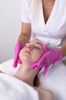 Female Patient Receives Spa Facial Massage Treatment In Spa Salon. Relax And Stress Relief. Professional Skin Care Therapist Takes Care Of Woman. Top View. Vertical Plane