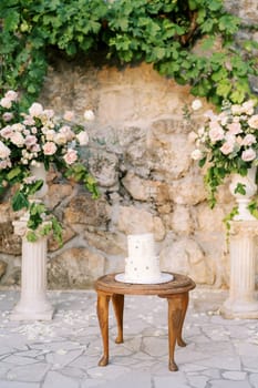 Wedding cake stands on a wooden table near a wedding semi-arch near a stone wall in the garden. High quality photo