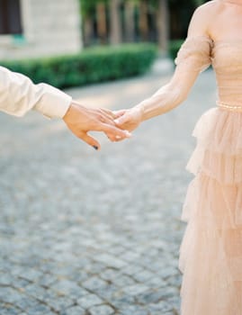 Bride holds groom fingers while standing on the paving stones in the garden. Cropped. Faceless. High quality photo