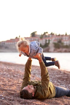 Dad is lying on the beach holding a little girl above him in outstretched arms. High quality photo