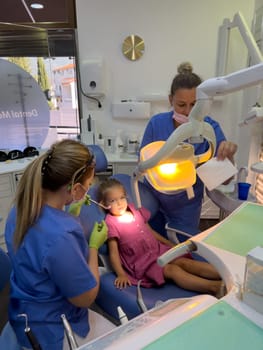 Dentist is going to examine a little girl sitting in a dental chair. High quality photo
