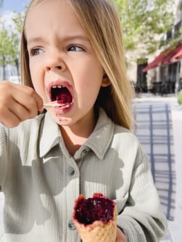 Little girl with stained mouth eating popsicles with a spoon. High quality photo