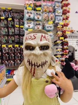 Little girl in the store trying on a scary zombie mask. High quality photo