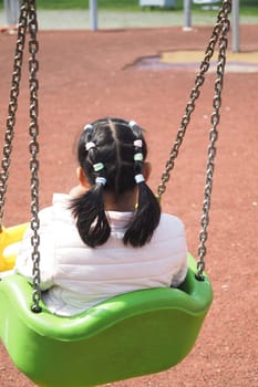 child having fun on a swing on the playground in public park