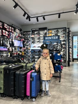 Little girl in sunglasses stands near travel suitcases in a store. High quality photo