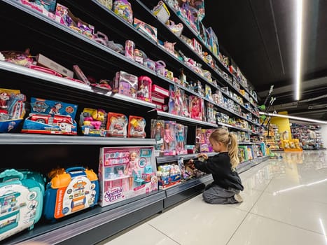 Little girl is sorting through toys on a shelf in a store while sitting on her knees. High quality photo
