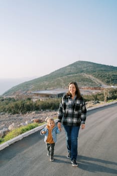 Smiling mother with little girl walking along the road in the mountains holding hands. High quality photo