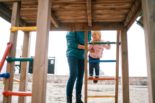 Mom supports a little girl climbing the stairs to the slide. Cropped. High quality photo