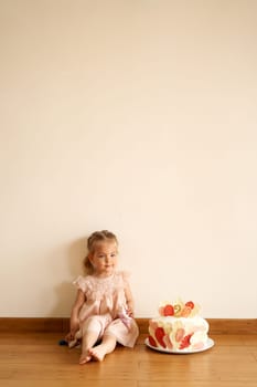 Little smiling girl with a doll sits on the floor next to a birthday cake. High quality photo