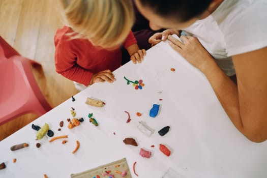 Mom with a little girl are looking at a plasticine flower on the table. Top view. High quality photo