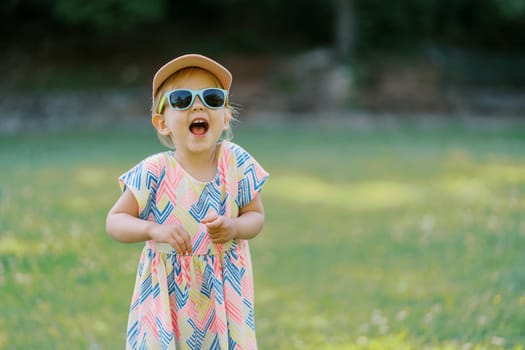 Little laughing girl stands in sunglasses on a sunny lawn. High quality photo