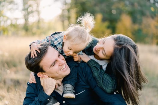 Mom and little girl look into the face of a laughing dad hugging him from behind. High quality photo