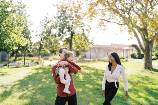 Dad holding a laughing little girl in his arms next to a standing smiling mom. High quality photo