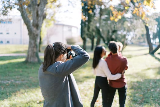 Girl-photographer takes pictures of parents with a little girl in their arms. Back view. High quality photo