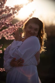 Woman blooming peach orchard. Against the backdrop of a picturesque peach orchard, a woman in a long white dress enjoys a peaceful walk in the park, surrounded by the beauty of nature