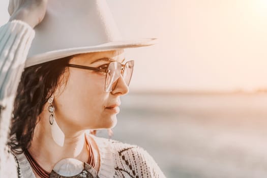 Portrait of a curly haired woman in a white hat and glasses on the background of the sea