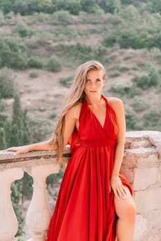 Woman red dress. Summer lifestyle of a happy woman posing near a fence with balusters over the sea