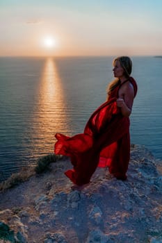 Woman sunset sea red dress, back view a happy beautiful sensual woman in a red long dress posing on a rock high above the sea on sunset