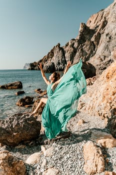 Woman green dress sea. Woman in a long mint dress posing on a beach with rocks on sunny day. Girl on the nature on blue sky background