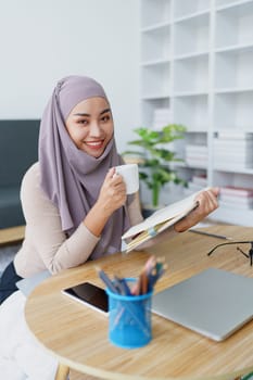 Muslim undergraduate student drinks coffee while read studying at home