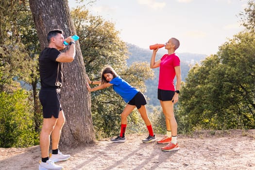 family resting and drinking water after sports in nature, concept of family outdoor activities and healthy lifestyle