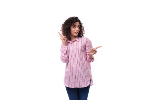 young authentic caucasian woman with curly black hair dressed in a pink shirt on a white background with copy space.