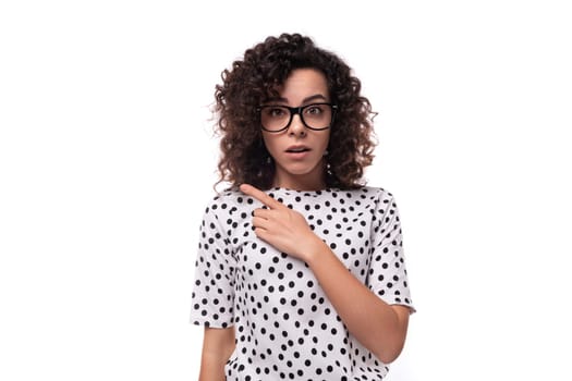 portrait of a surprised young curly brunette well-groomed slim lady wearing a polka-dot shirt with short sleeves.