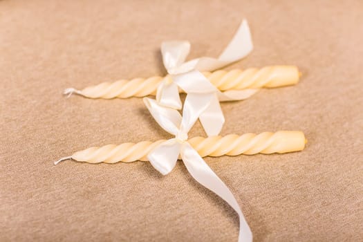 Two white candles with ribbons on a beige background