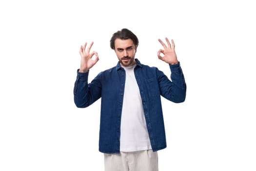 handsome young brunette man in a denim shirt gesturing with his hands on a white background.