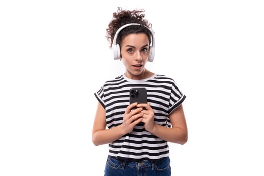 young music lover curly brunette lady with black hair dressed in a striped t-shirt listens to music in wireless headphones.