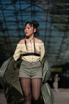 A beautiful Asian woman in shorts and a green leather coat comes out of the subway