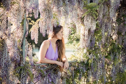 Woman wisteria lilac dress. Thoughtful happy mature woman in purple dress surrounded by chinese wisteria.