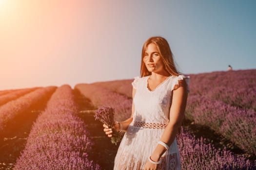 Close up portrait of young beautiful woman in a white dress and a hat is walking in the lavender field and smelling lavender bouquet.