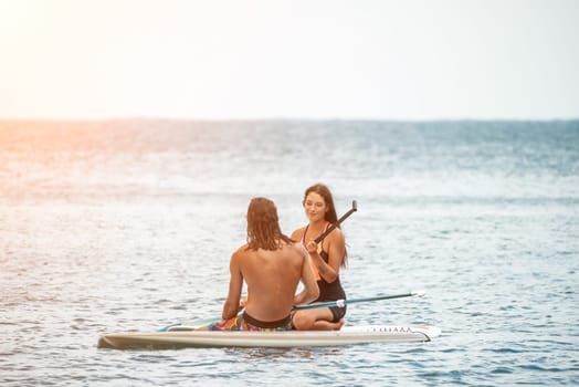 Sea woman and man on sup. Silhouette of happy young woman and man, surfing on SUP board, confident paddling through water surface. Idyllic sunset. Active lifestyle at sea or river