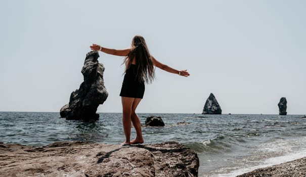 Woman travel sea. Young Happy woman in a long red dress posing on a beach near the sea on background of volcanic rocks, like in Iceland, sharing travel adventure journey