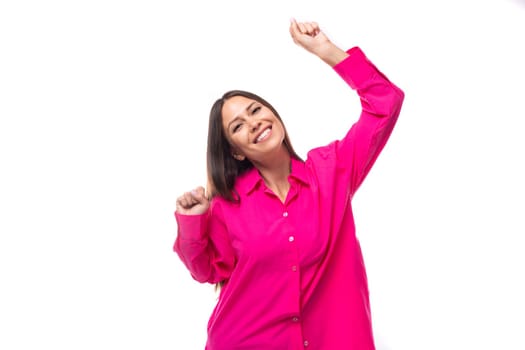 happy positive young brunette lady dressed in a bright pink shirt on a white background.