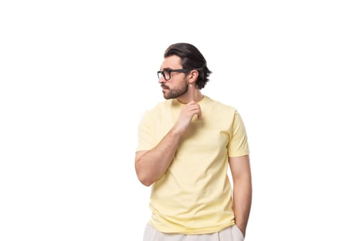 attractive young brunette man with a beard in a yellow t-shirt wears eyeglasses.