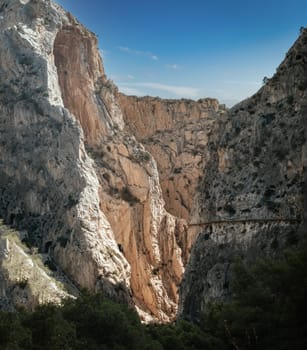 Tourists navigate the slender trails of Caminito del Rey beside parallel train tracks.