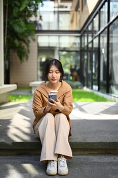 Portrait of pretty young Asian woman sitting front of business center and using mobile phone.