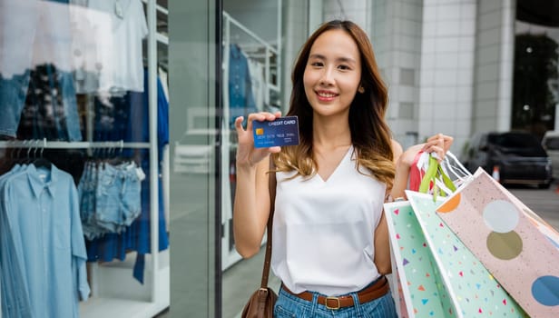 A young woman smiles with shopping bags and a credit card in her hand. She's a smart shopper who knows how to find the best deals and rewards at the mall.