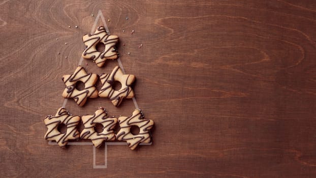 Christmas tree form made from star-shaped cookies with chocolate, banner on the brown wooden background with copy space