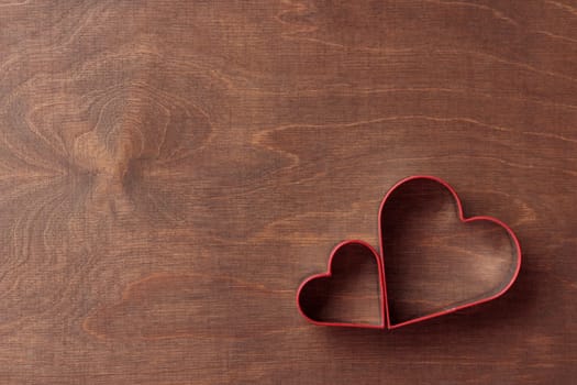 Two heart-shaped cookie cutters on the dark brown wooden background, horizontal banner, top view