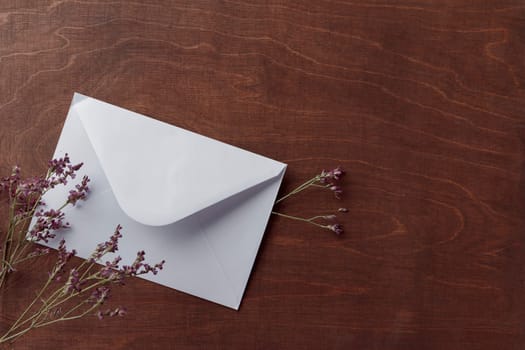 Wooden rustic brown background with white letter envelope with dried flowers