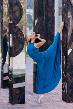 Beautiful asian ballerina in blue dress and pointe shoes posing outdoors