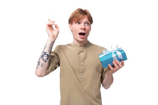 young cute caucasian guy with red hair holding a colorful box with a gift.
