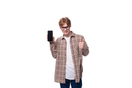 a young caucasian guy with red hair in glasses and a plaid shirt shows the screen of a smartphone. advertising concept.